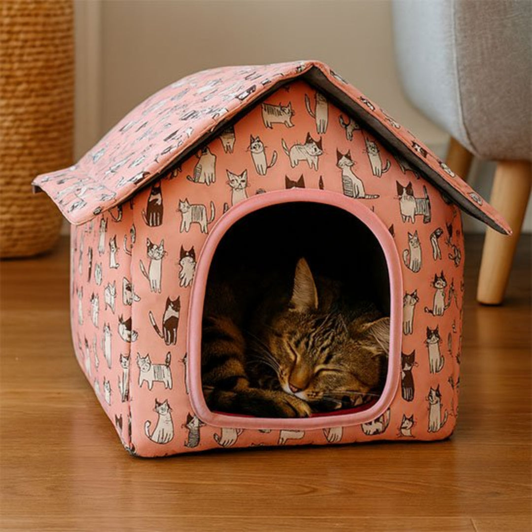 Chat tigré endormi à l'intérieur d'une niche pour chat extérieur rose saumon à motifs de chats