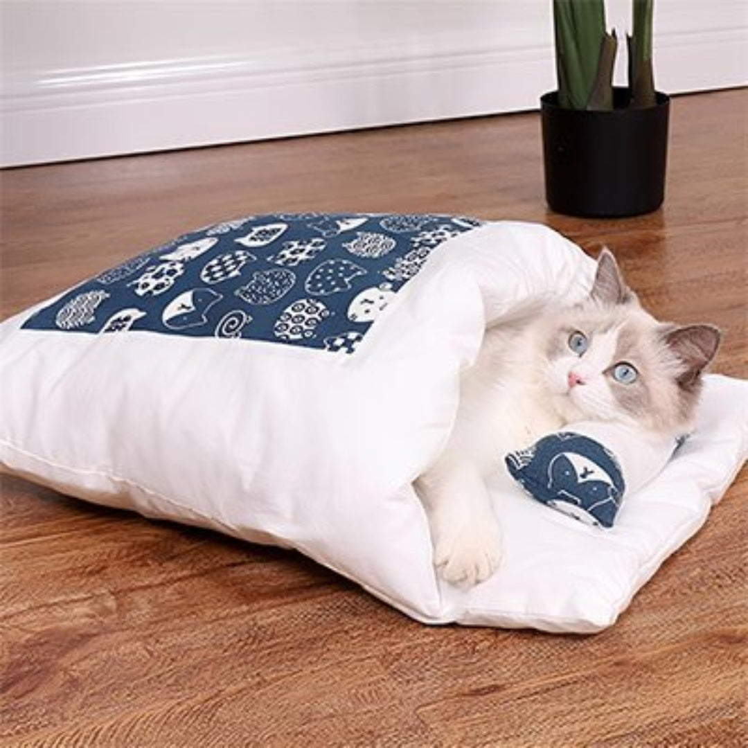 Chat allongé dans un lit pour chat blanc et bleu avec motif de chats posé sur plancher en bois