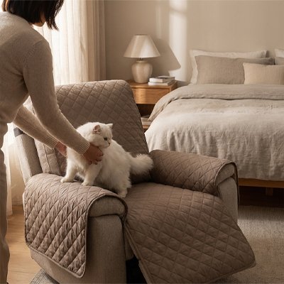 Une personne installe un chat blanc à poil long sur un fauteuil beige protégé par une une protection canapé chat, dans une chambre.