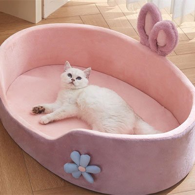 Chat blanc allongé dans un panier chat en peluche rose et mauve orné d'oreilles de lapin