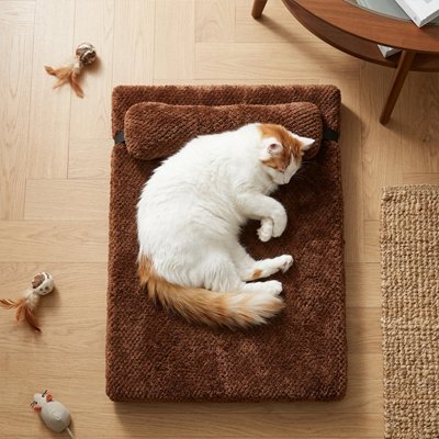 Chat blanc et roux endormi sur un lit chat marron avec appui-tête, vue de haut.