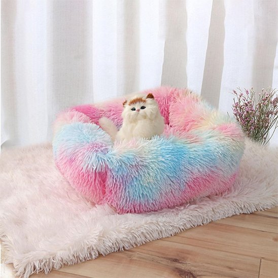 Chat en peluche blanc installé dans un panier chat aux couleurs pastel dégradées (rose, bleu, jaune)