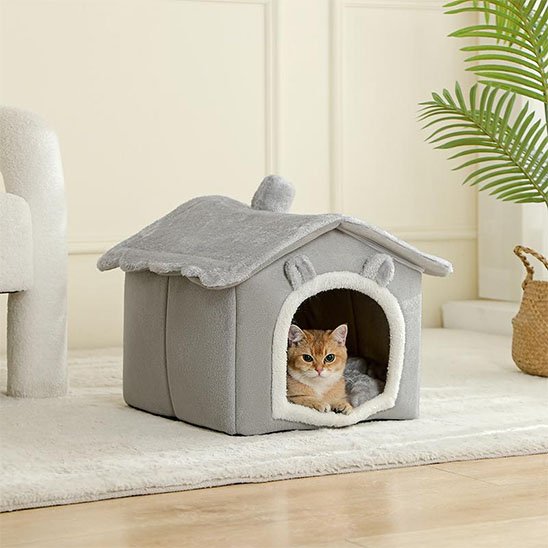 Chat roux allongé paisiblement à l'intérieur d'une niche pour chat en peluche grise
