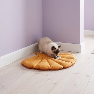 Chat s'étirant sur un tapis chat design en forme de feuille jaune