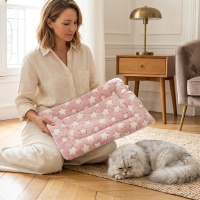 Femme assise par terre présente un tapis chat rose à motifs d'étoiles blanches.