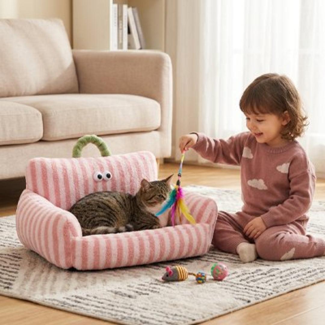 Un enfant fait jouer un chat tigré couché dans un panier rose et blanc à rayures avec un plumeau