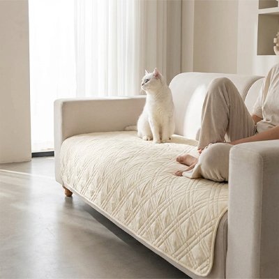 Protection canapé chat beige matelassé avec un chat blanc assis dessus.