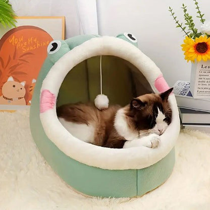 un chat bicolore dort paisiblement en boule à l'intérieur d'une niche pour chat en forme de grenouille, posée sur un tapis blanc moelleux