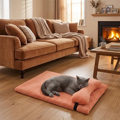 Un chat gris dort paisiblement sur un lit chat de couleur rose, posé sur un parquet en bois