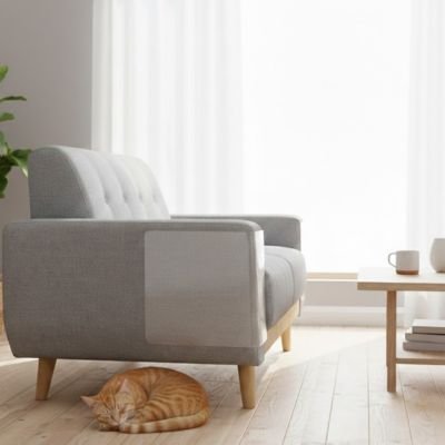 Un chat roux dort paisiblement sur le plancher sous un canapé gris moderne dont l'accoudoir est protégé par Protege canape chat 