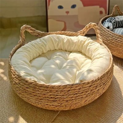 Un panier chat osier tissé de forme ronde avec un coussin blanc moelleux posé un un tapis