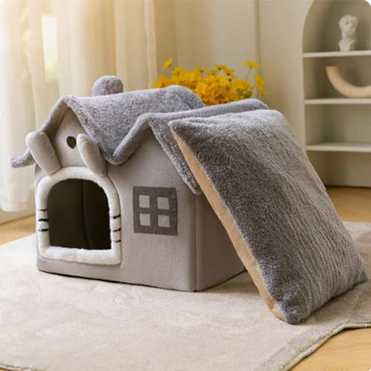 Un panier pour chat en forme de petite maison grise posé sur un tapis