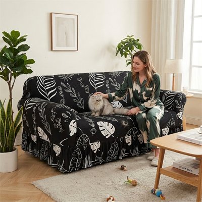 Une femme caresse un chat à poils longs gris et blanc allongé sur un protege canape chat noire à motifs de feuilles tropicales blanches