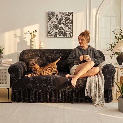 Une femme est assise sur un canapé recouvert d'un protege canape chat noire à effet marbré blanc