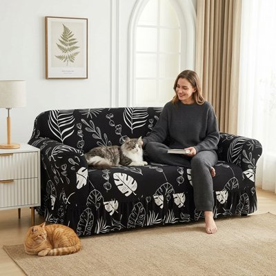 Une femme est assise sur un canapé recouvert d'un protege canape chat noire à motifs de feuilles tropicales blanches