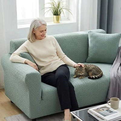 Une femme est assise sur une housse canapé chat verte et caresse son chat