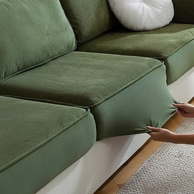 Une personne étire une protection canapé chat élastique de couleur verte sur un coussin de canapé sectionnel