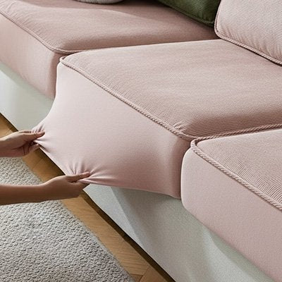 Une personne étire une protection canapé chat élastique de couleur rose dragée sur un coussin de canapé sectionnel